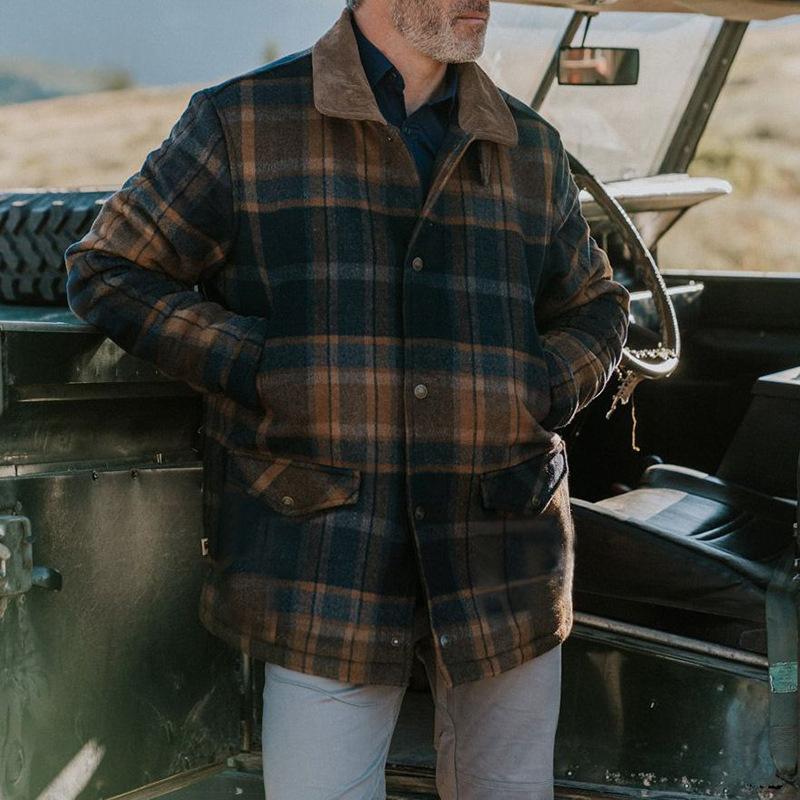 A man wearing a brown and navy blue plaid wool jacket with a tan collar, standing next to a vintage green vehicle outdoors.