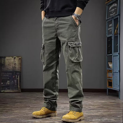 A person wearing olive green cargo pants, a black sweatshirt, and yellow boots, standing in a room with a gray wall, wooden floor, and blue lockers.