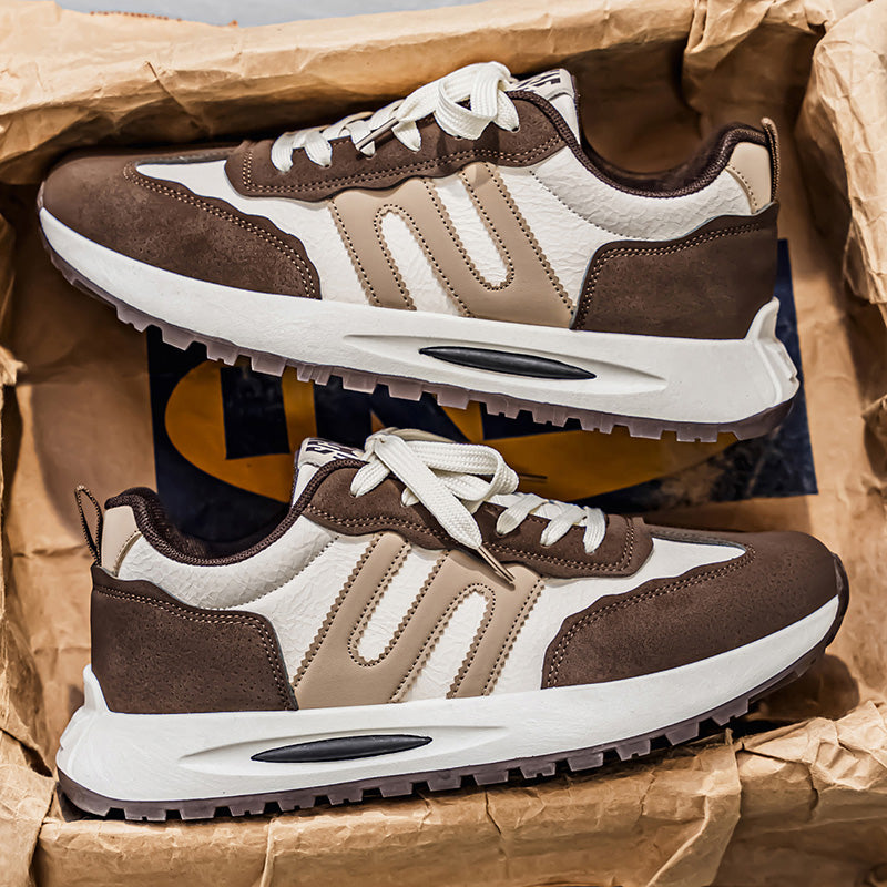 A pair of low-top athletic sneakers in brown, beige, and white, displayed inside a brown paper box.