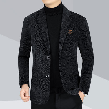 A man wearing a dark charcoal gray textured blazer over a black turtleneck sweater and black trousers, shown from the neck down against a light gray studio background.