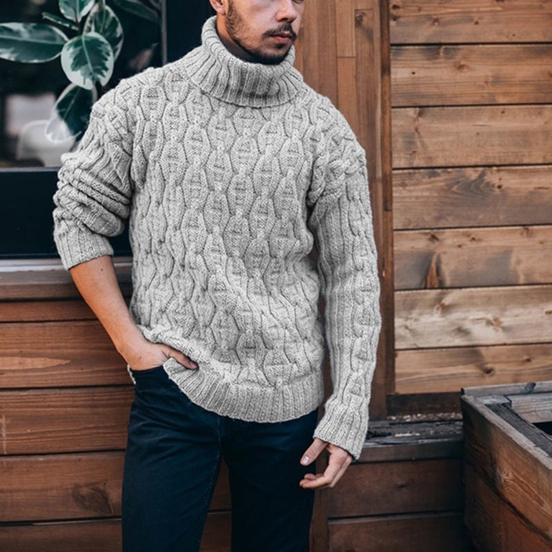 Man wearing a cable knit sweater standing against a wooden wall.