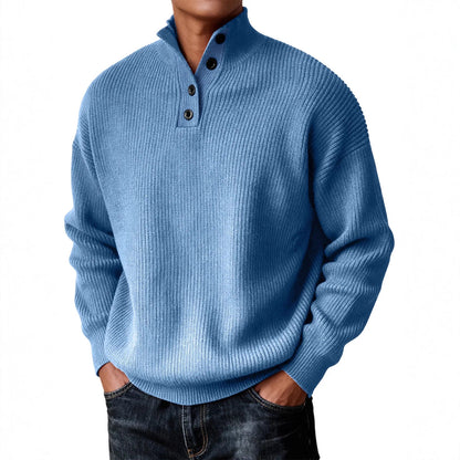 A man wearing a light blue ribbed knit mock-neck sweater with three dark buttons, paired with dark jeans, against a plain white background.