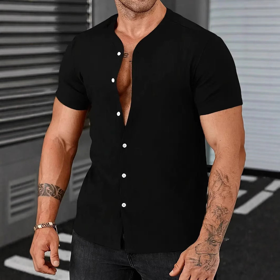 Man wearing a black short-sleeve button-up shirt with tattoos on arms, standing against a metallic background.