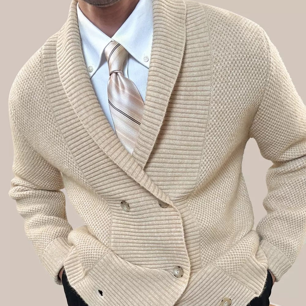 A man wearing a cream-colored textured knit double-breasted cardigan over a white dress shirt and a beige striped tie, shown from the neck down against a solid light beige background.