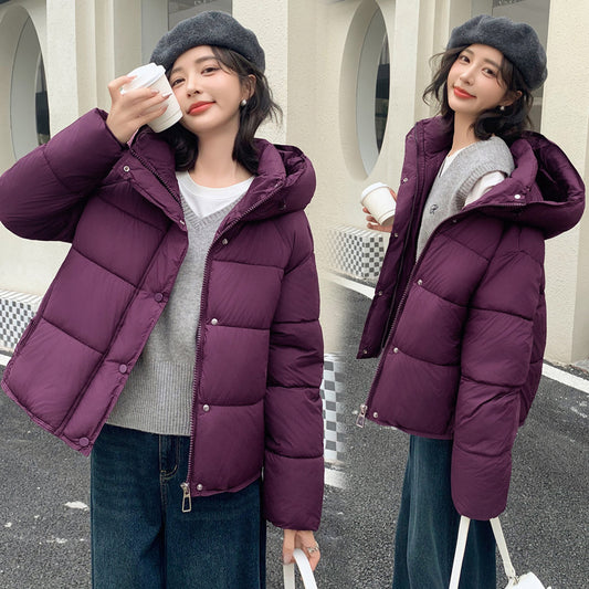 Two women modeling a plum purple hooded puffer jacket outdoors. The jacket has horizontal quilting, a front zipper with snap buttons, and a large hood.