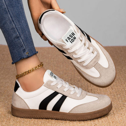 White and beige sneakers with black stripes worn by a person on a neutral background