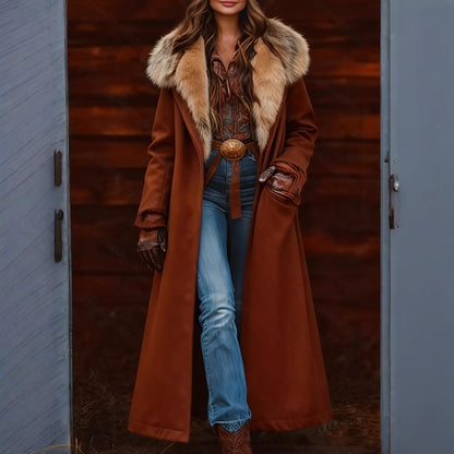 A woman models a long brown coat with a beige fur-trimmed collar, styled with blue jeans, a brown belt, and brown boots, standing in front of a rustic wooden door.