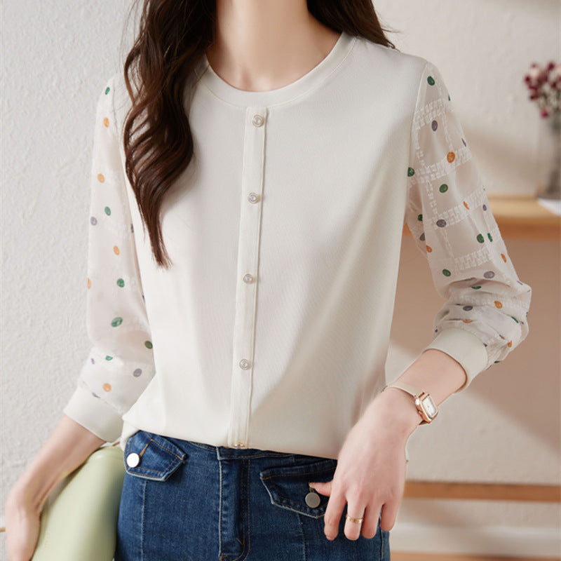 A woman wearing a cream-colored blouse with sheer patterned sleeves and a button-down front, paired with blue jeans.