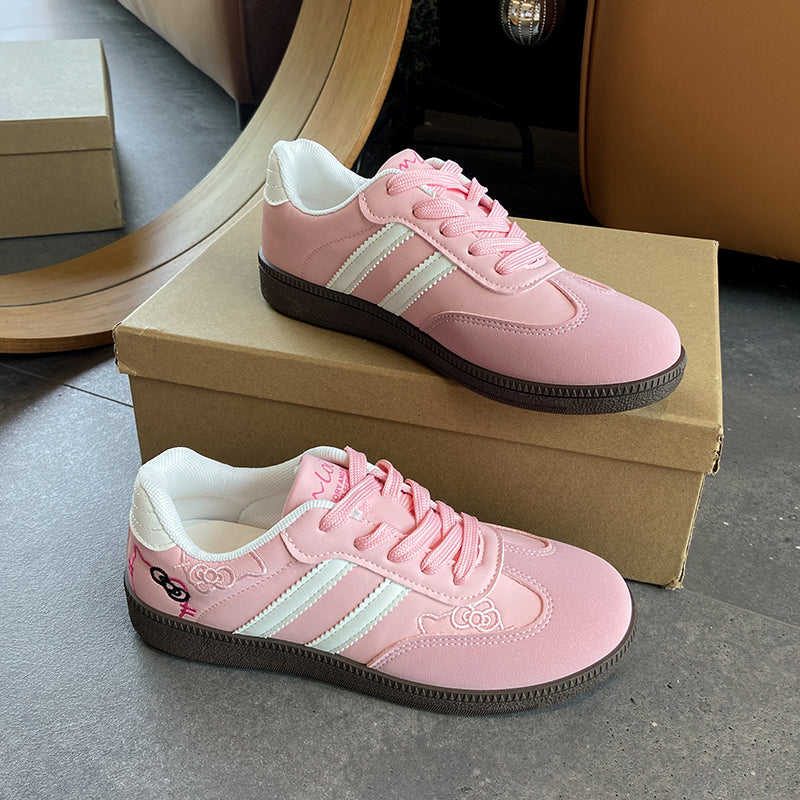 A pair of pink low-top sneakers with white side stripes, pink laces, and dark brown soles, displayed on and around a brown shoebox on a gray floor.